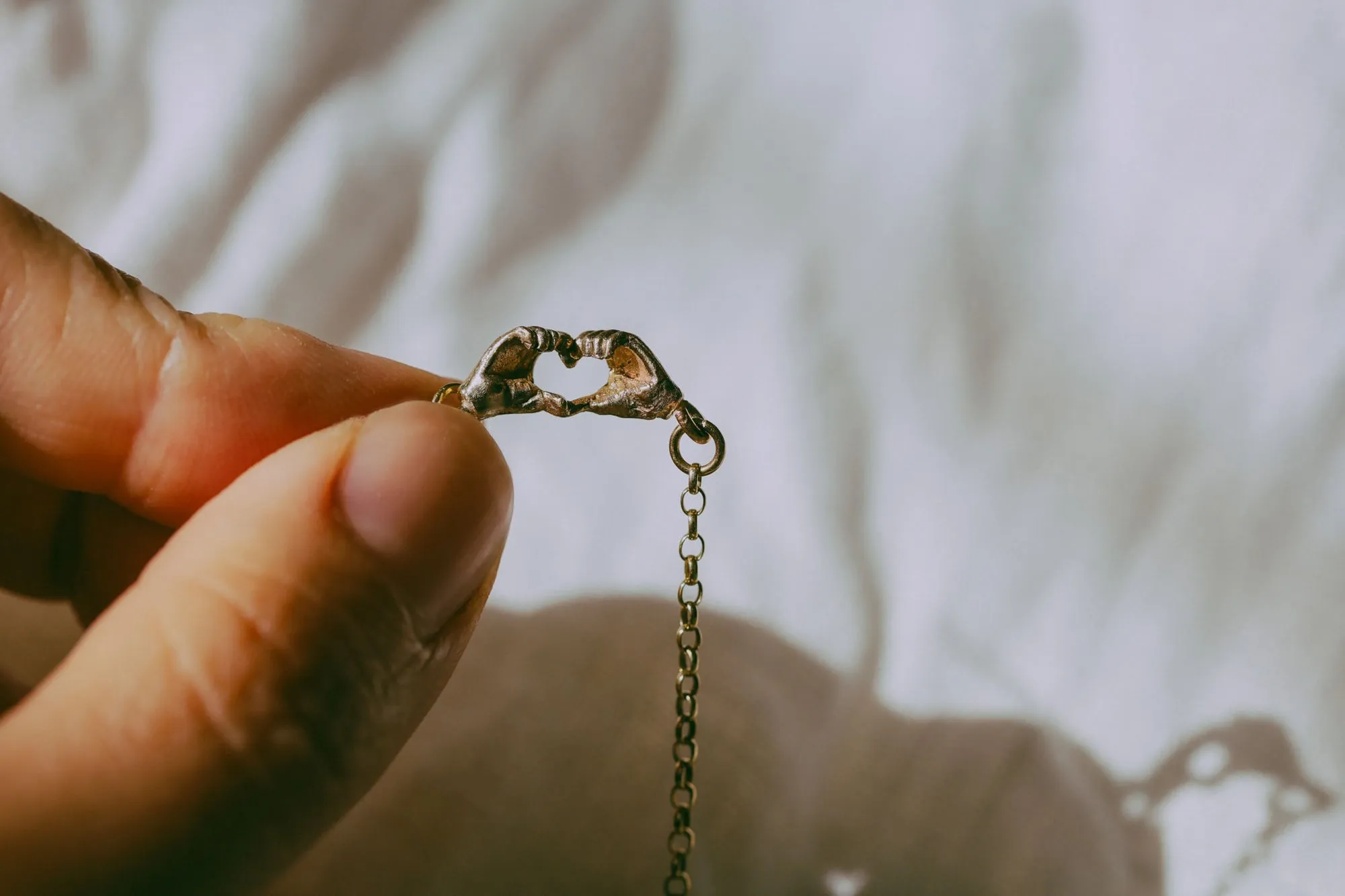 Two hands forming a heart around a gold pendant, held up to soft window light