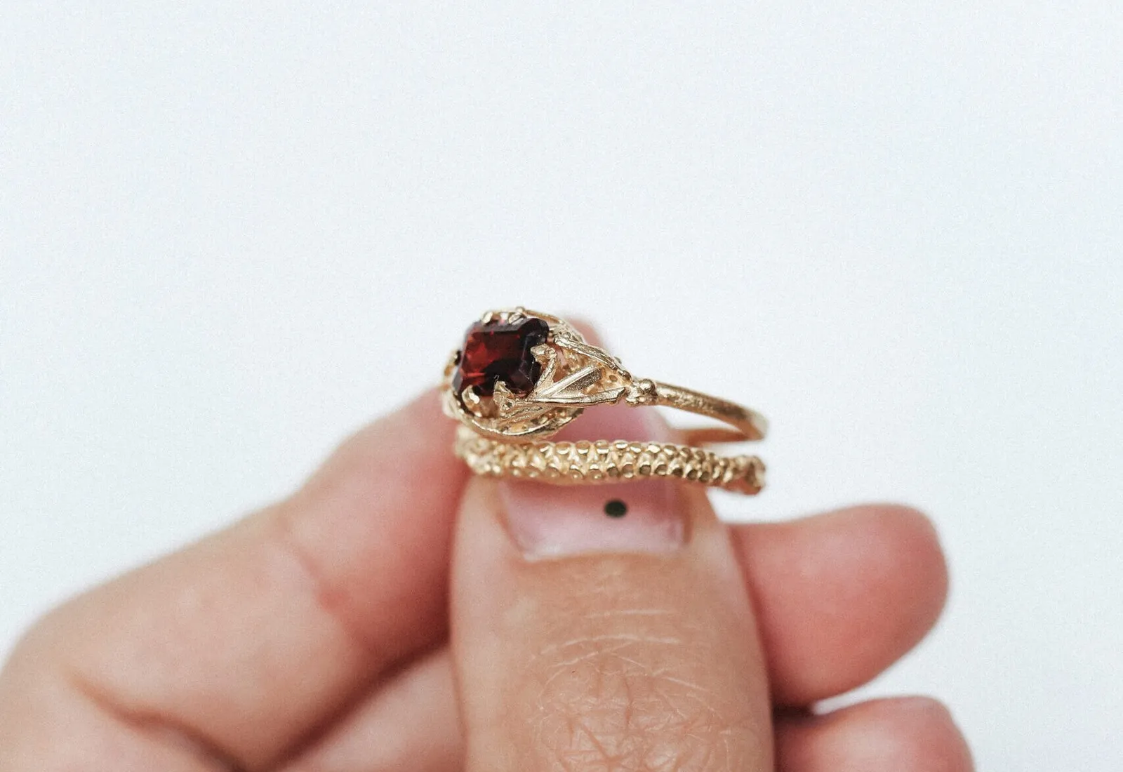 A vintage-style gold engagement ring set with a deep red garnet, worn on a fingertip