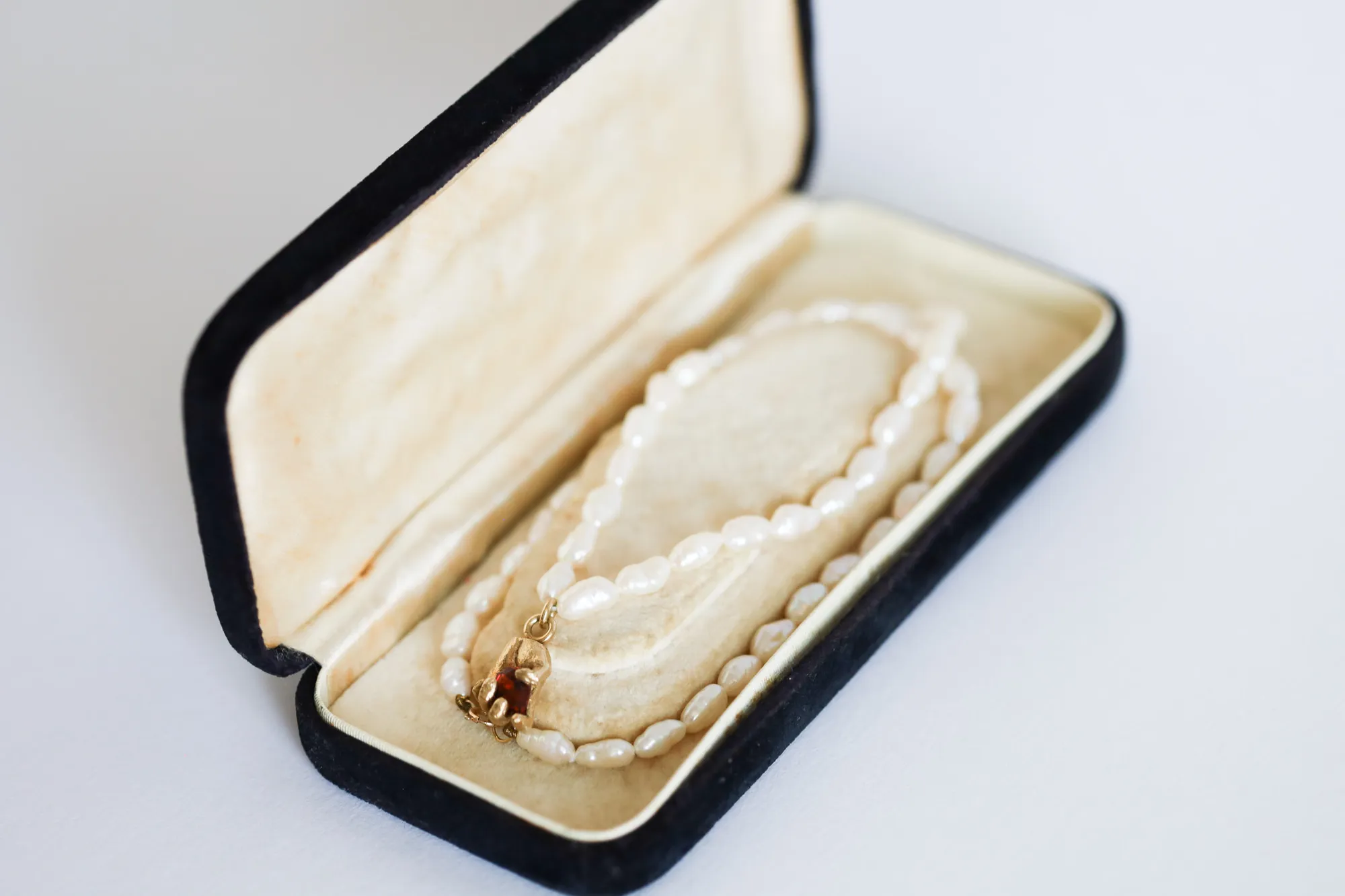 A strand of small freshwater pearls with a gold hand-and-garnet clasp, resting in an open vintage jewellery box
