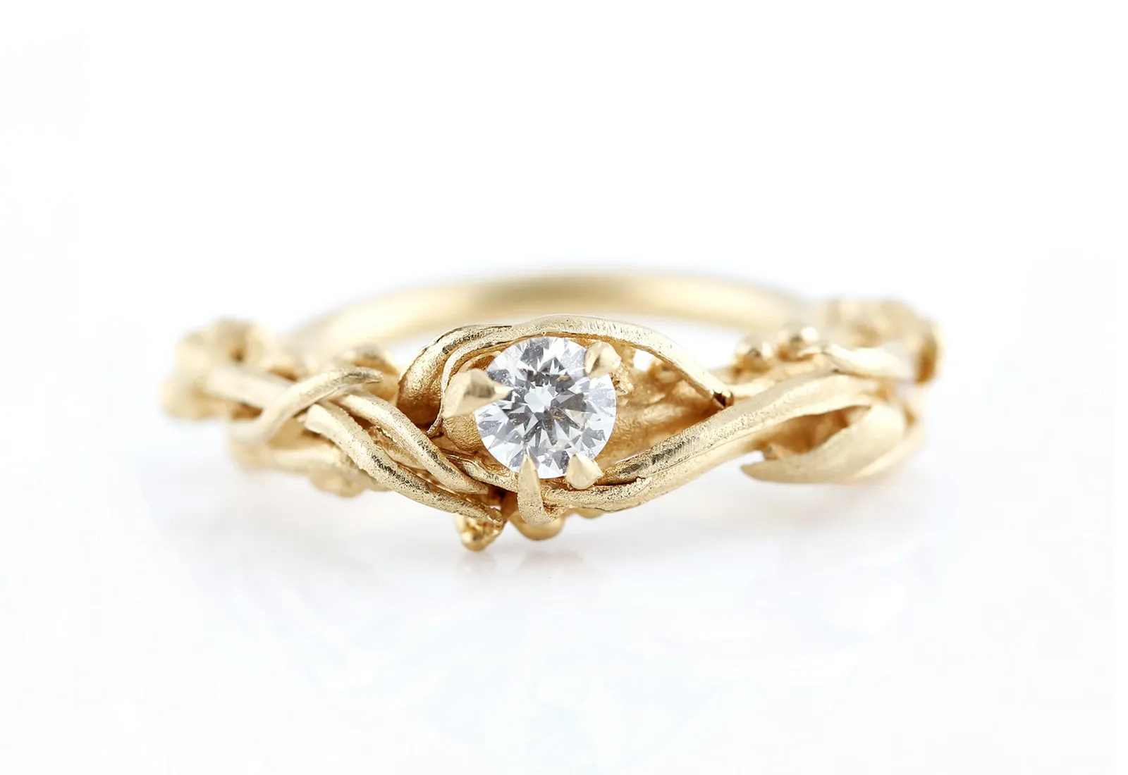 A hand-textured gold engagement ring with an entwined twig-like band, set with a round brilliant diamond